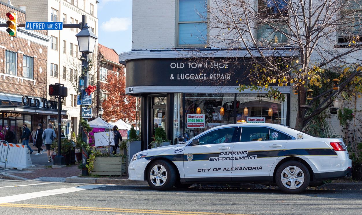 Alexandria, VA, USA 11-28-2020: A view of downtown Alexandria with shops and people on street. A white police car used by Parking Enforcement Officers is parked on the street in front of shops.