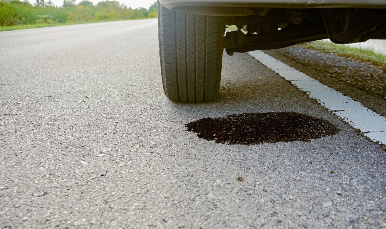 Close-up of dirty engine oil leaking under a broken-down car on the side of the road. Old engine oil stains on the road, Car repair and maintenance concept