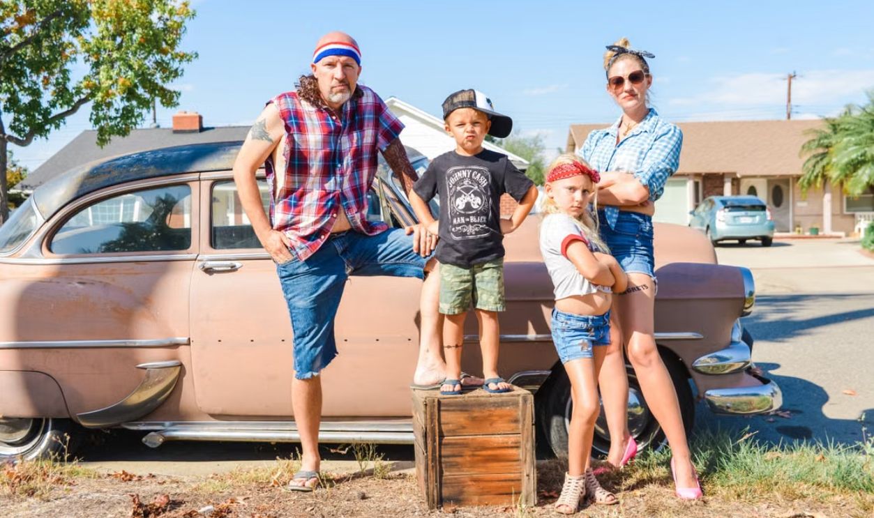 Family of four with retro style posing by a vintage car on a sunny day.