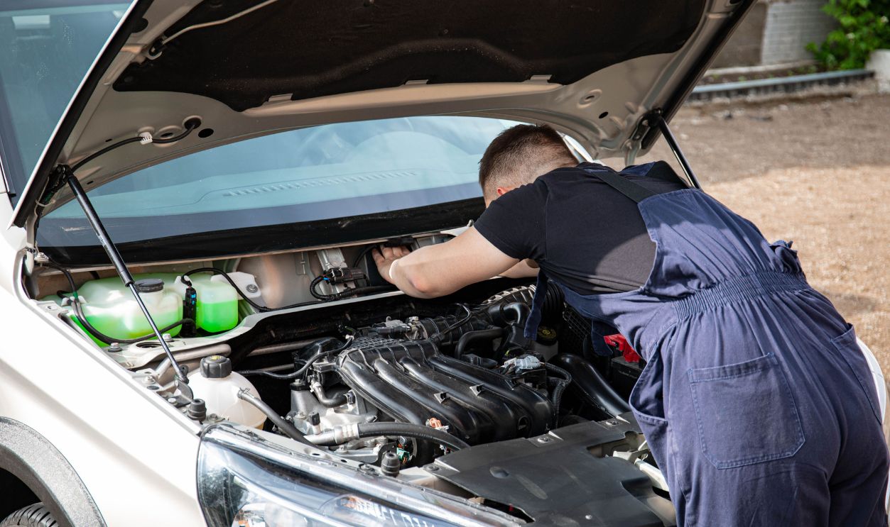 A skilled mechanic works on a car engine in an outdoor setting, showcasing automotive maintenance.