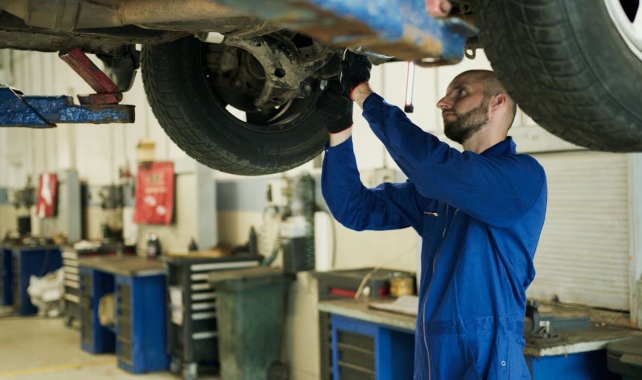 Man in Blue Work Clothes Fixing a Car