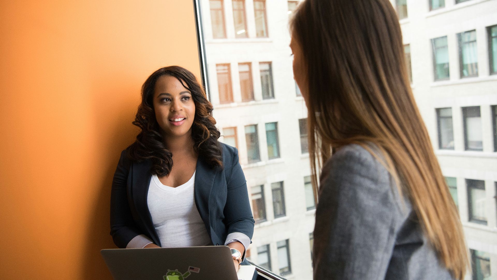 woman standing infront of woman holding laptop