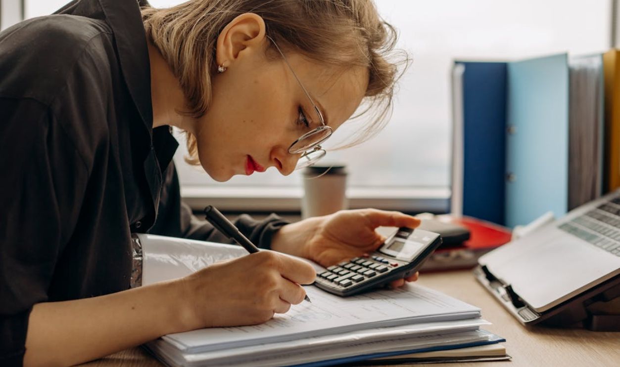 A Woman Writing on a Book while Holding a Calculator
