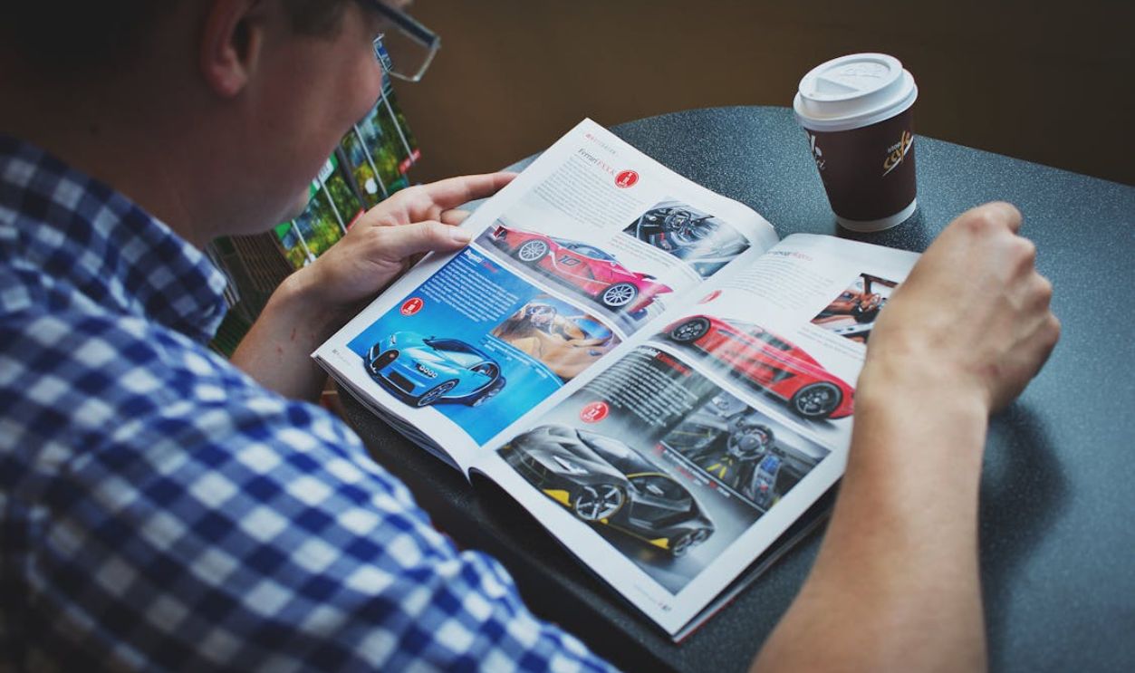 Man in Blue and White Gingham Print Shirt Reading Car Magazine