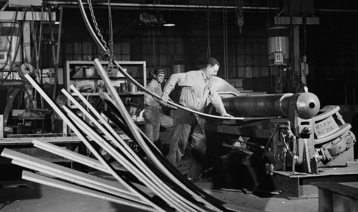 Rolling Steel steel mill employees rolling steel, with one man guiding steel through a rolling mill at an steelworks in Chicago, Illinois, circa 1955. Rolling is a process in which steel is rolled to reduce the thickness or create a uniform thickness. 