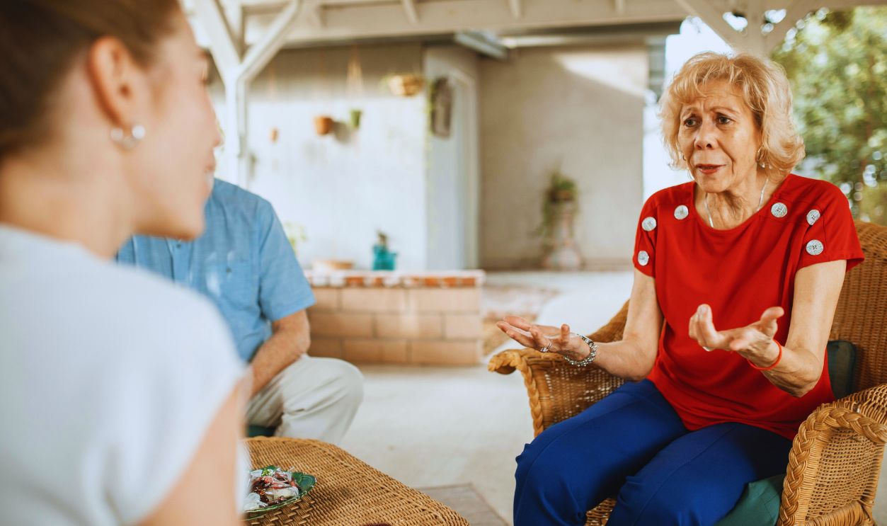 An Elderly Woman Sitting on a Woven Chair while Talking to Her Daughter