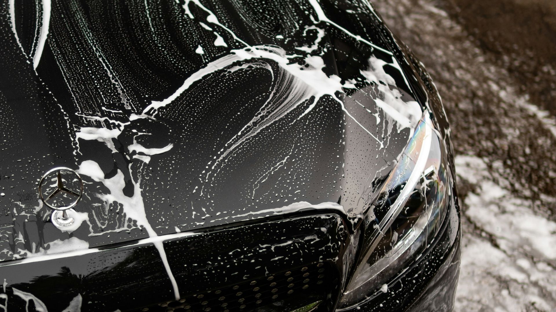 Black car covered in soap suds during wash.