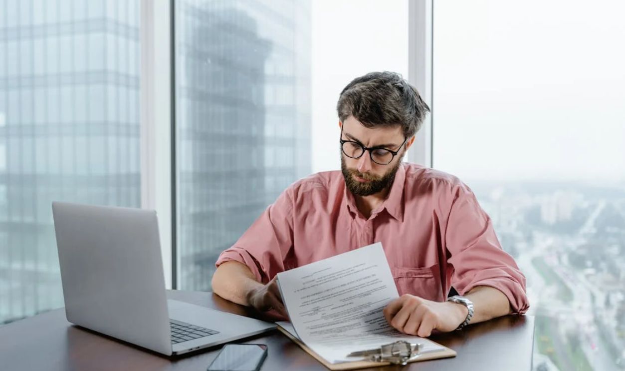 A Man in Pink Long Sleeves Wearing Eyeglasses while Looking at the Papers on the Table