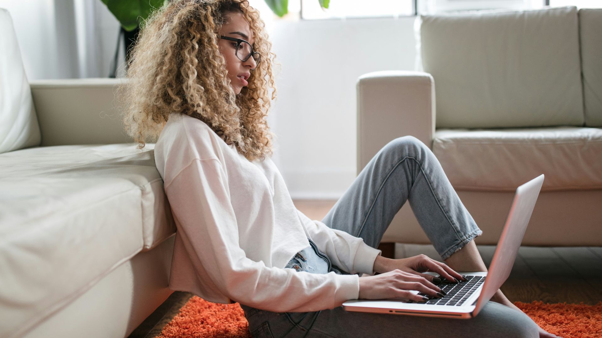 woman sitting on floor and leaning on couch using laptop