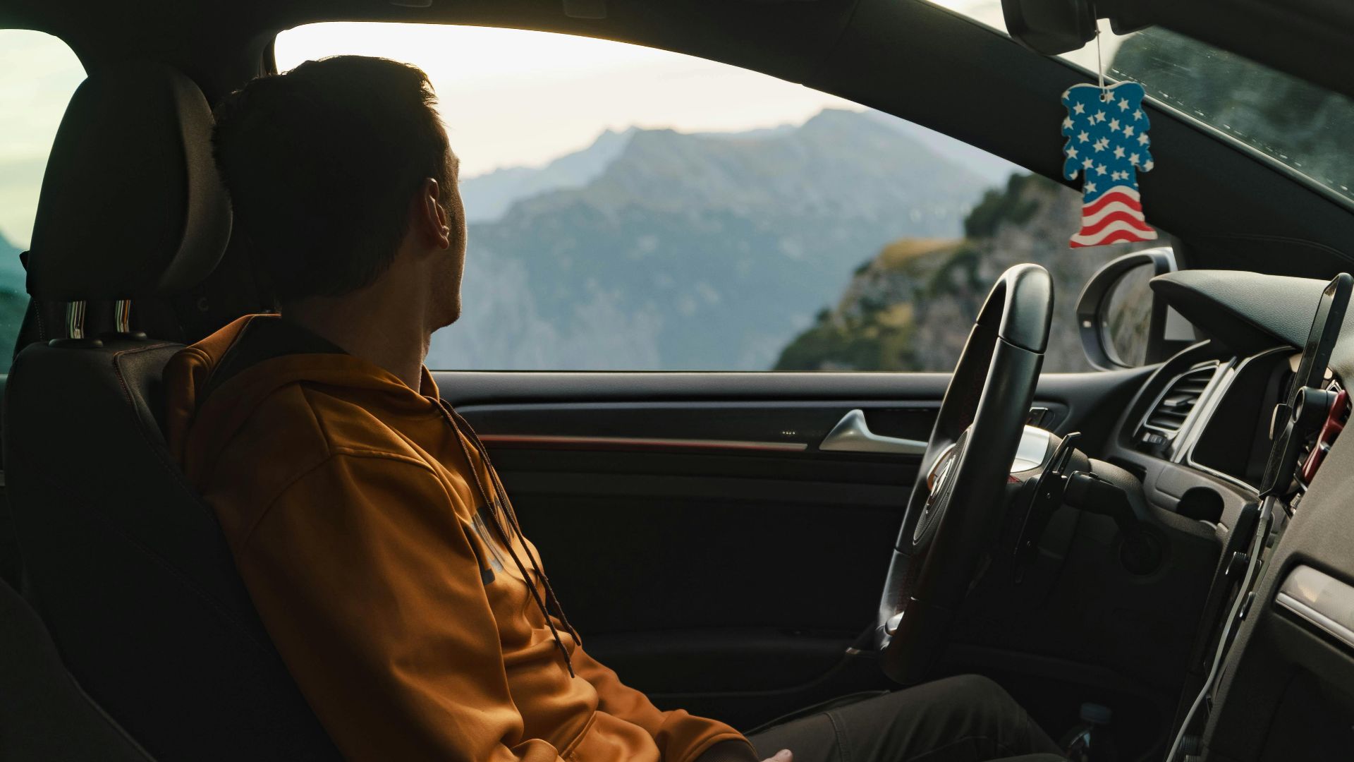A man in a car admires the scenic mountain view through the window, wearing a casual hoodie.