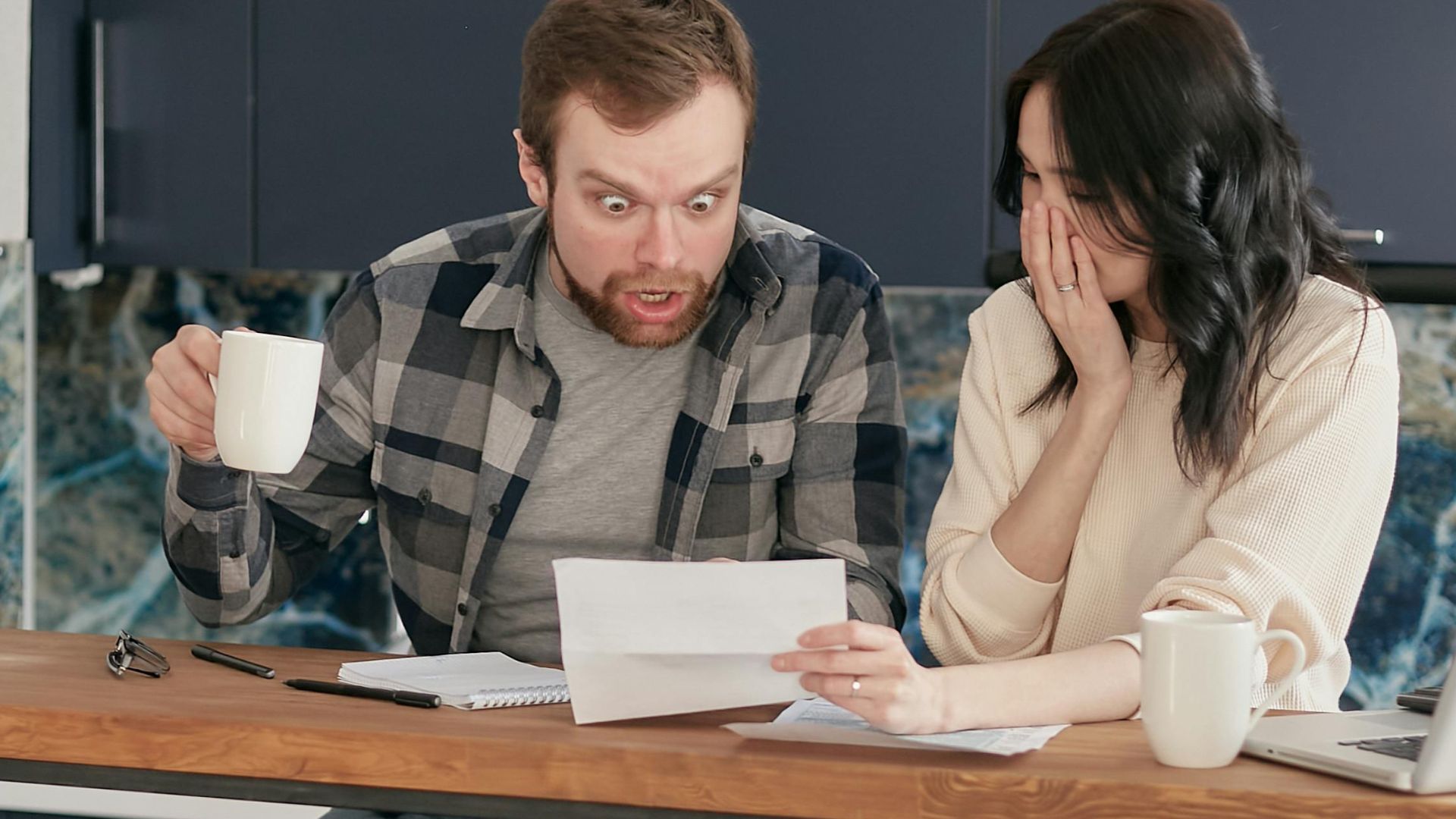 A worried couple reviewing financial documents at their kitchen table.