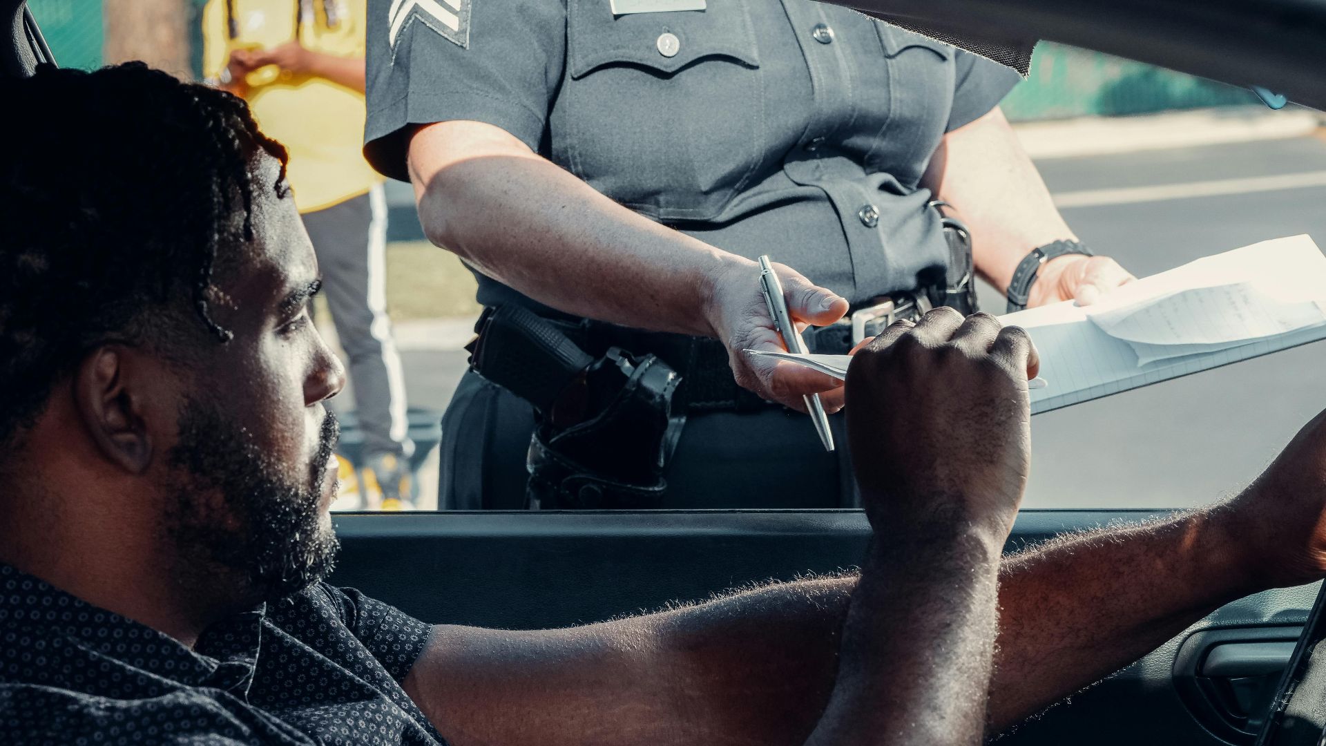 Police officer handing a traffic ticket to a driver during roadside inspection.