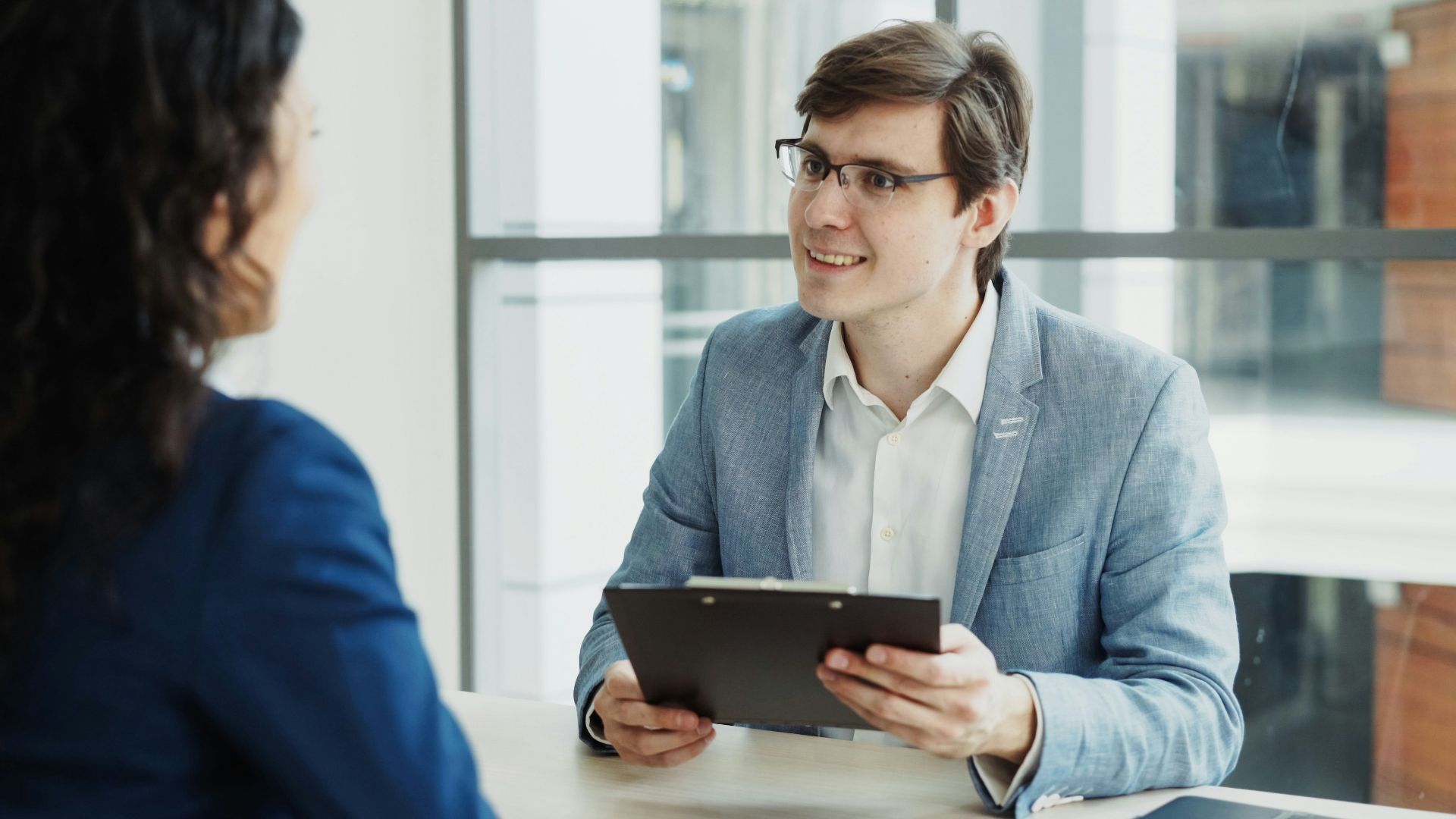 Man in suit interviews woman holding clipboard.