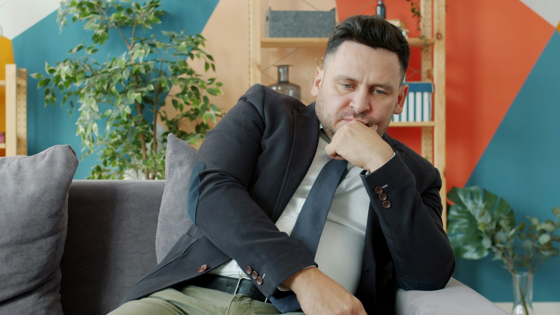 Man in suit sitting on couch looking thoughtful.