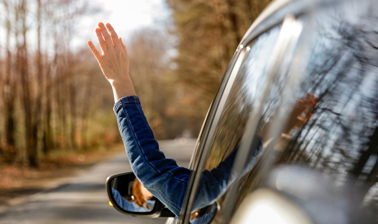 Close up of woman's hand waving out of a car window. Driving a car in a road on a sunny day.