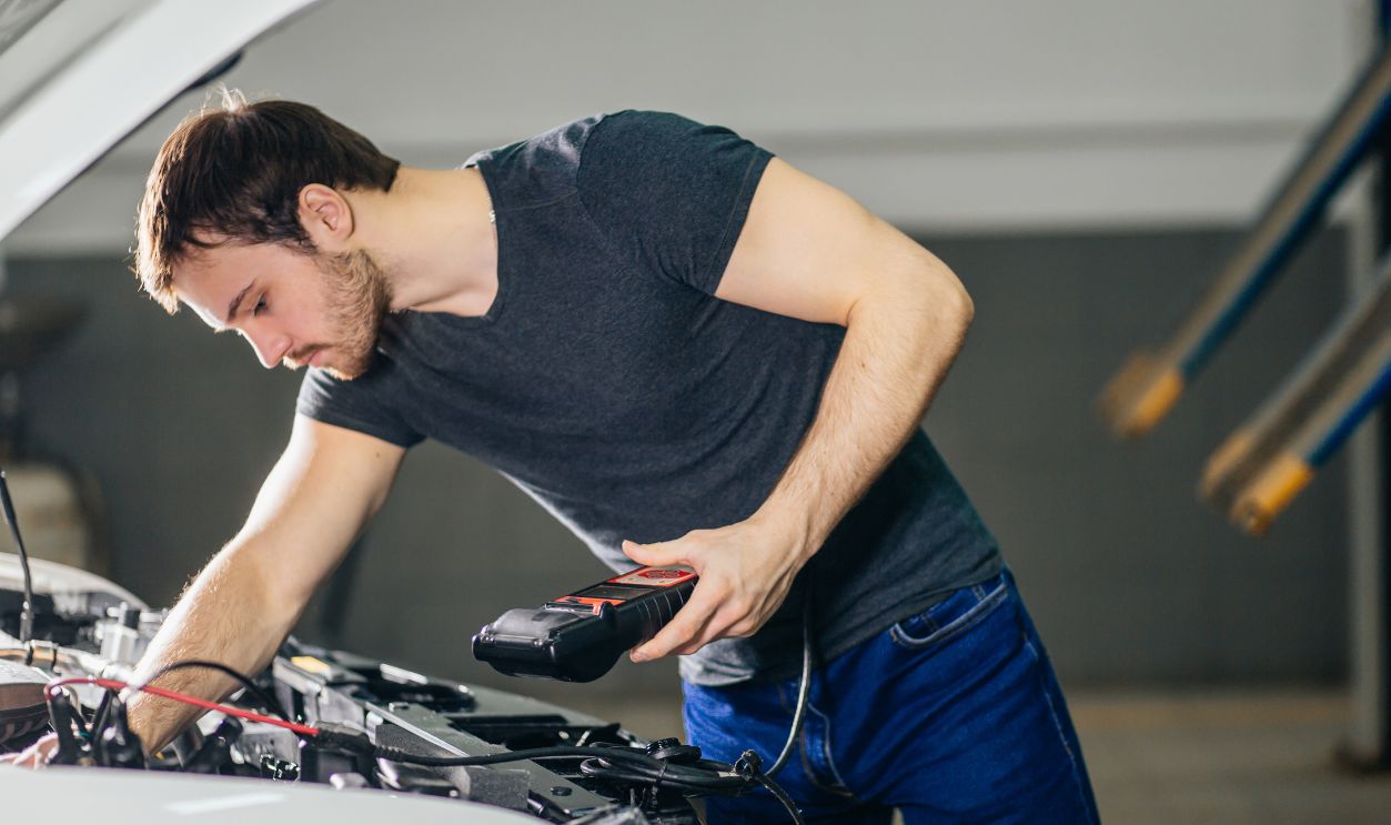 Car mechanic using electrical tool for testing car system in garage repair