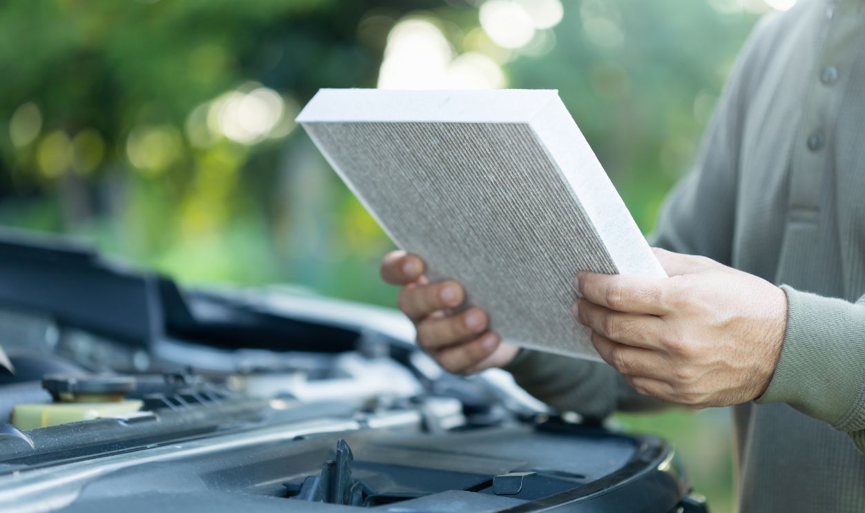  A car owner holds an air filter for examination. Importance of regular inspection, cleaning, and replacement of car air filters, Emphasizes maintenance for better air quality and vehicle efficiency