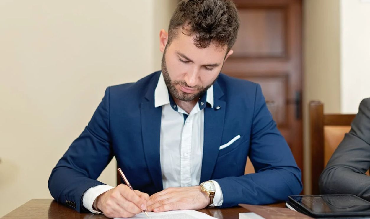 Man Sitting at a Table and Signing a Document