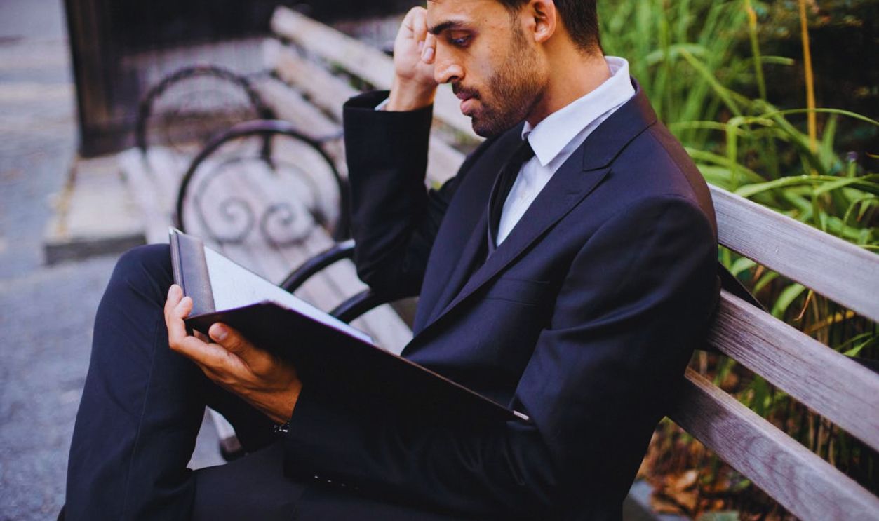 Man in Suit Sitting on Park Bench with a Black Folder