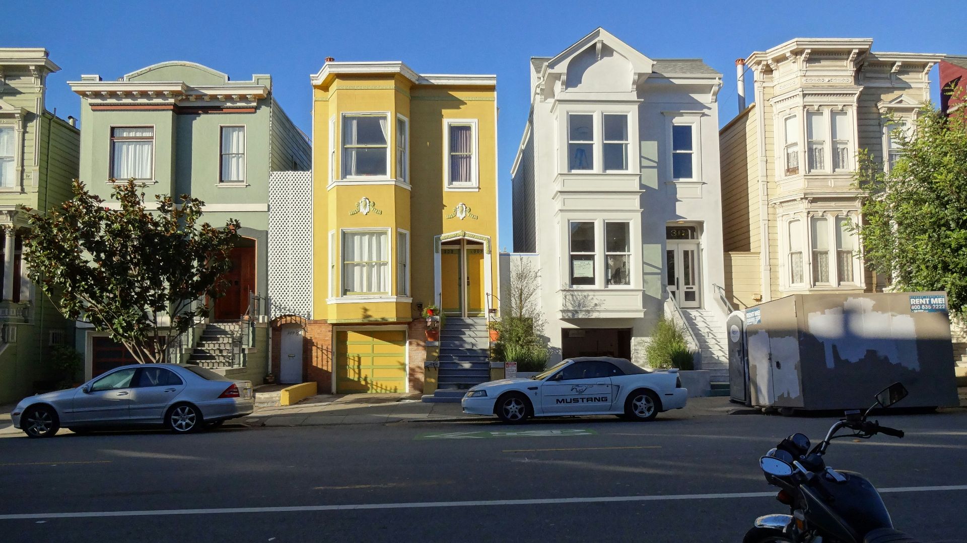 Colorful houses line a street with cars and motorcycle.