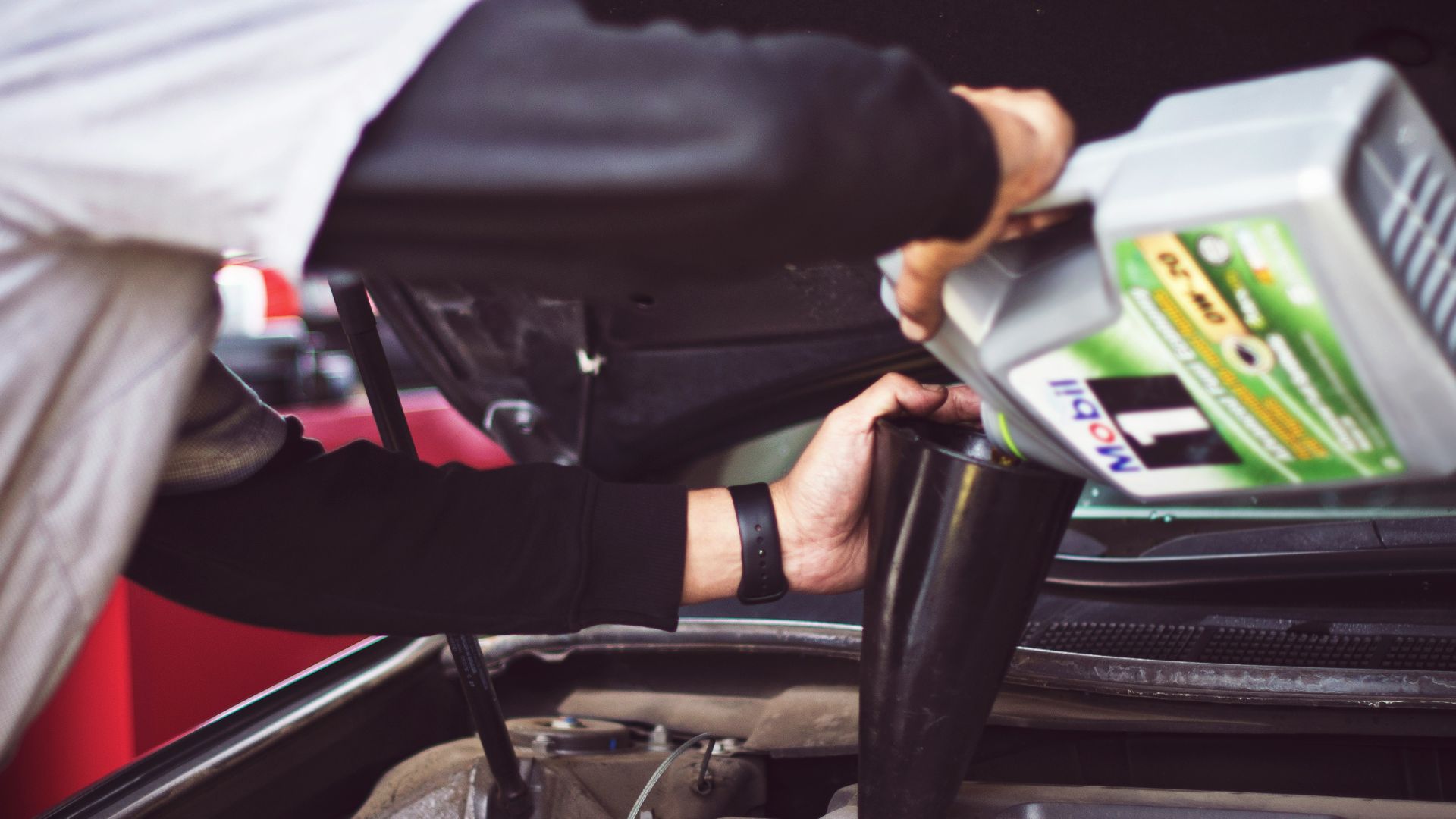 man refilling motor oil on car engine bay