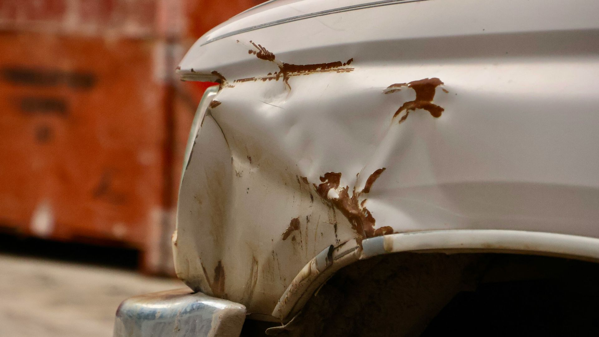 the front end of a white car with rust on it