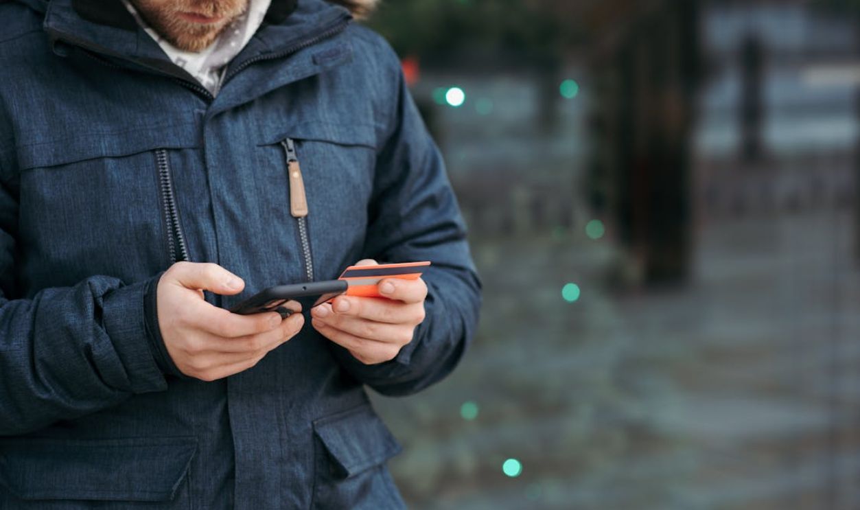 Man browsing smartphone and holding credit card on street