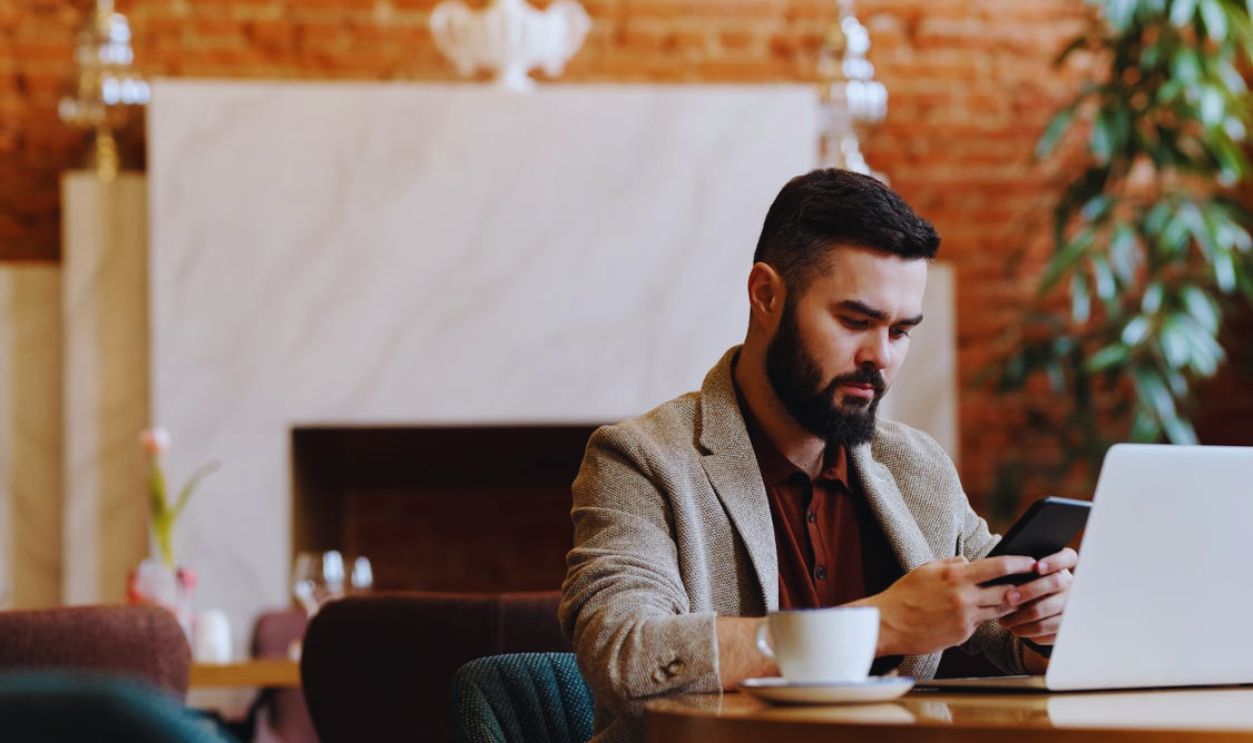 Man Sitting on Table with Laptop while Using Phone