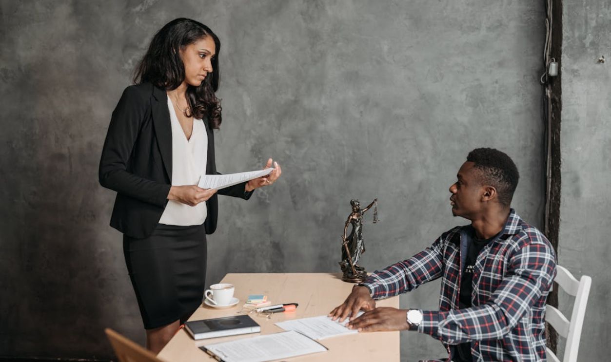 Woman Standing by Man with Documents on Desk