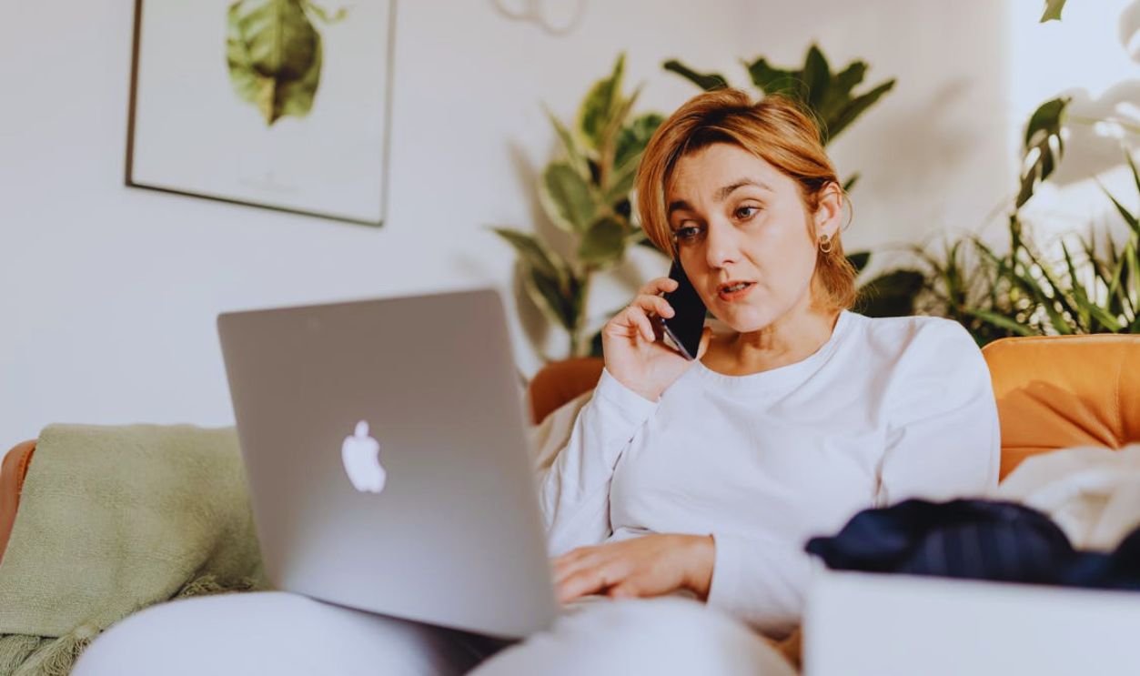Woman Sitting on a Couch Using Laptop and Talking Through the Phone