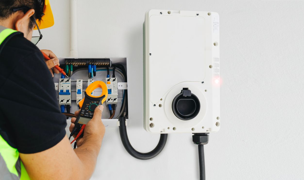 Close-up of an electrician performing tests with a clamp meter during home EV charger installation. Focusing on precision and safety for reliable electric vehicle charging. 