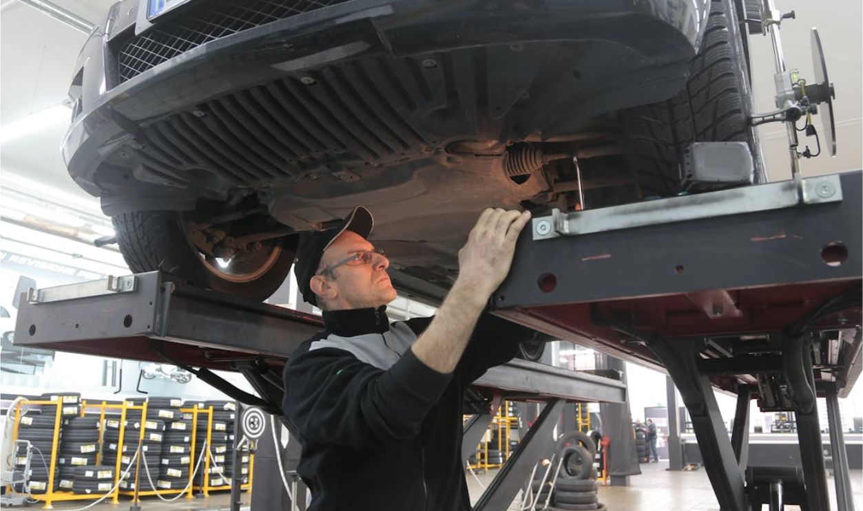 Man in Black Jacket Standing Under the Vehicle