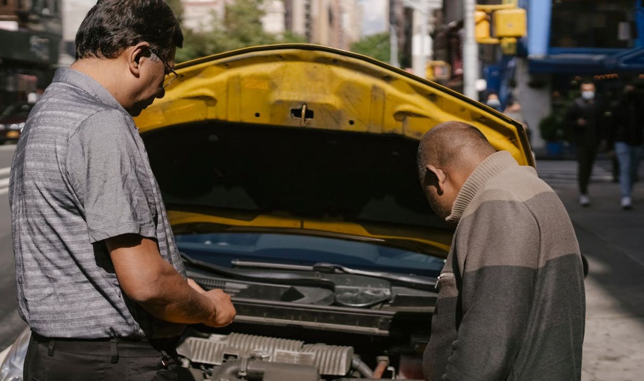 Ethnic mechanic checking car standing near man
