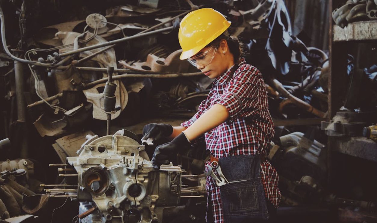 Woman Wears Yellow Hard Hat Holding Vehicle Part