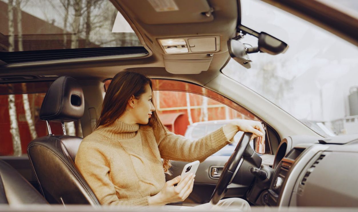 Adult woman sitting in car and using smartphone