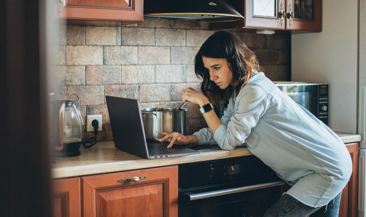 Woman in Blue Denim Jacket Holding Laptop While Cooking