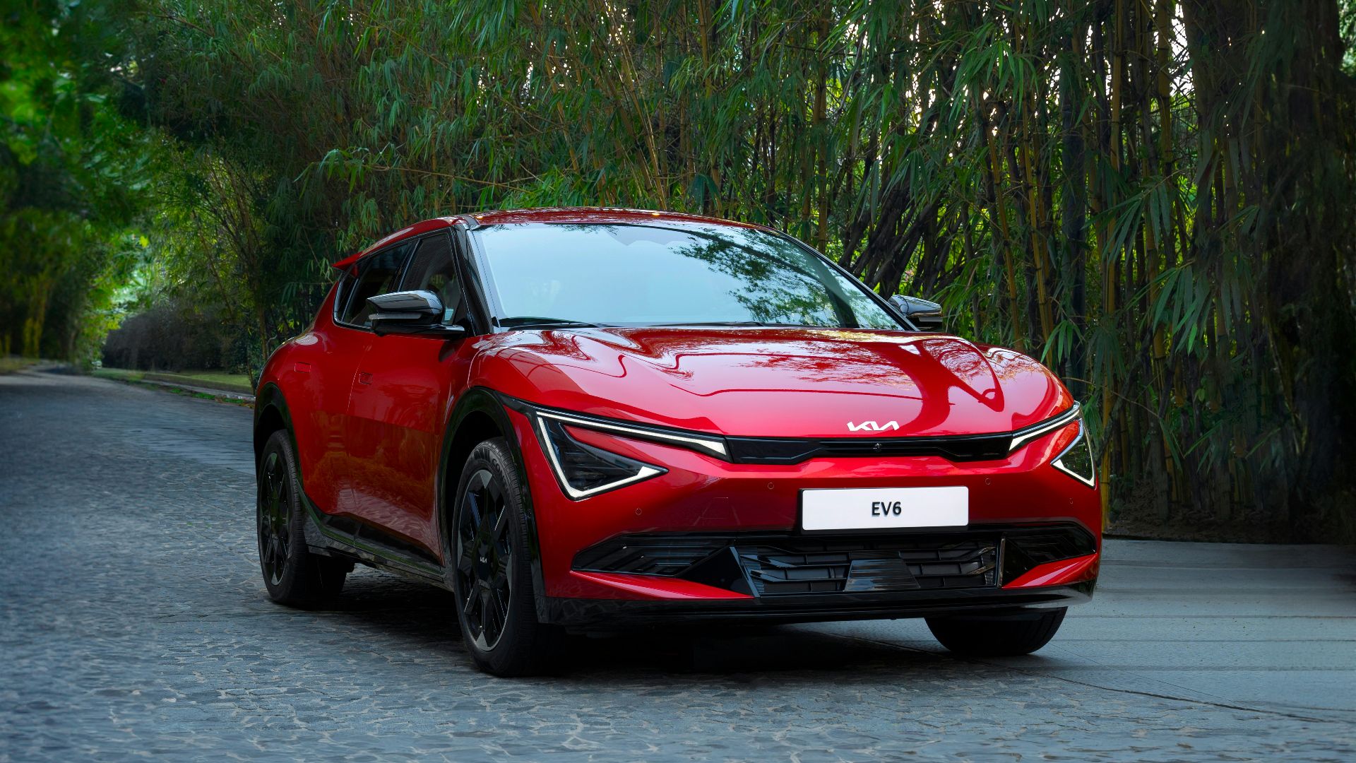 A red car driving down a street next to trees