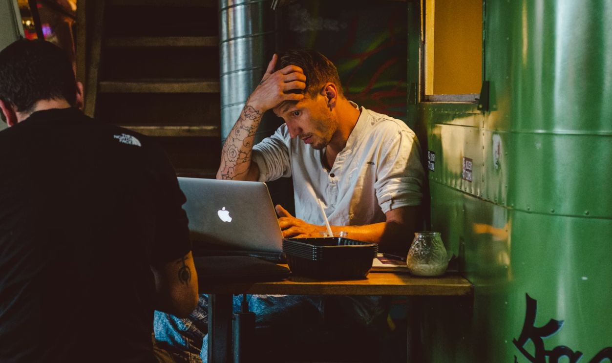 man in front of silver MacBook while scratching his head