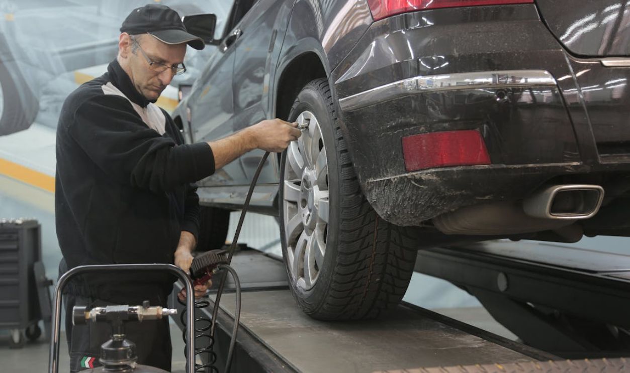 Serious car mechanic pumping up car wheel in modern service garage