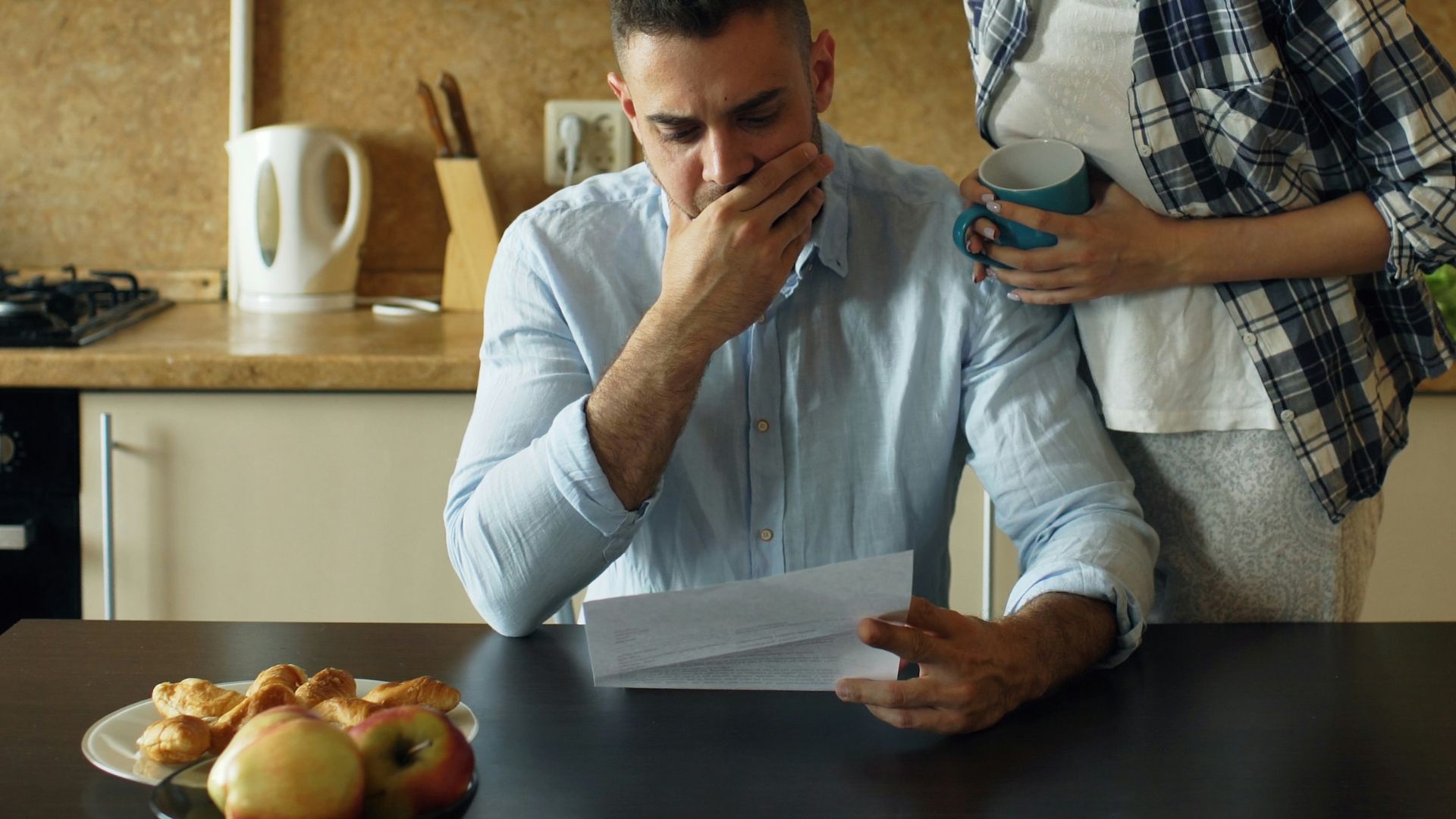 Couple looking stressed over bills at kitchen table.