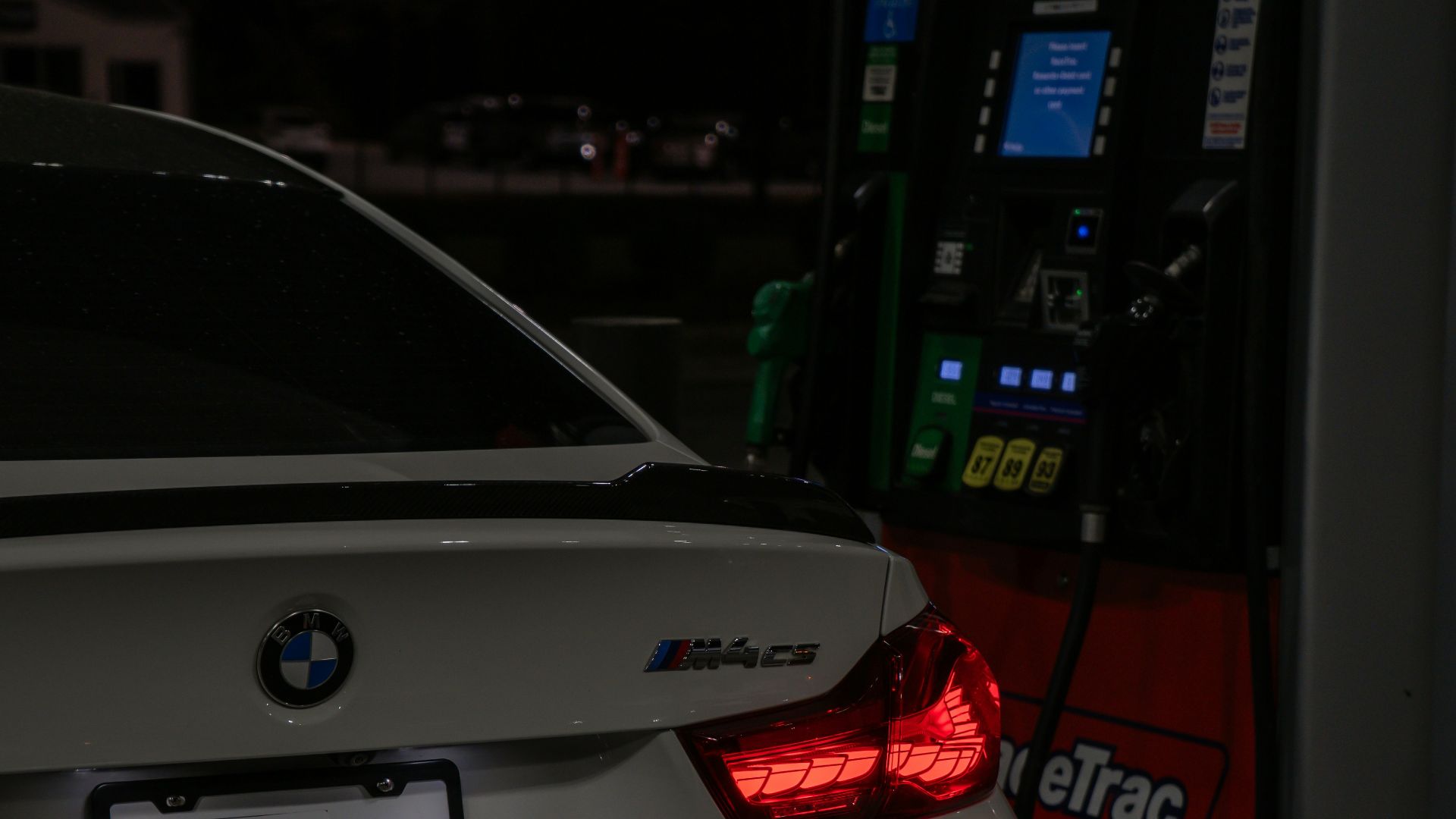 A white BMW m4 is refueling at night.