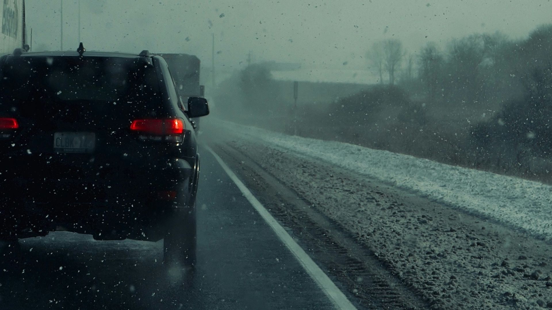 Cars driving on a wet road during a snowstorm.