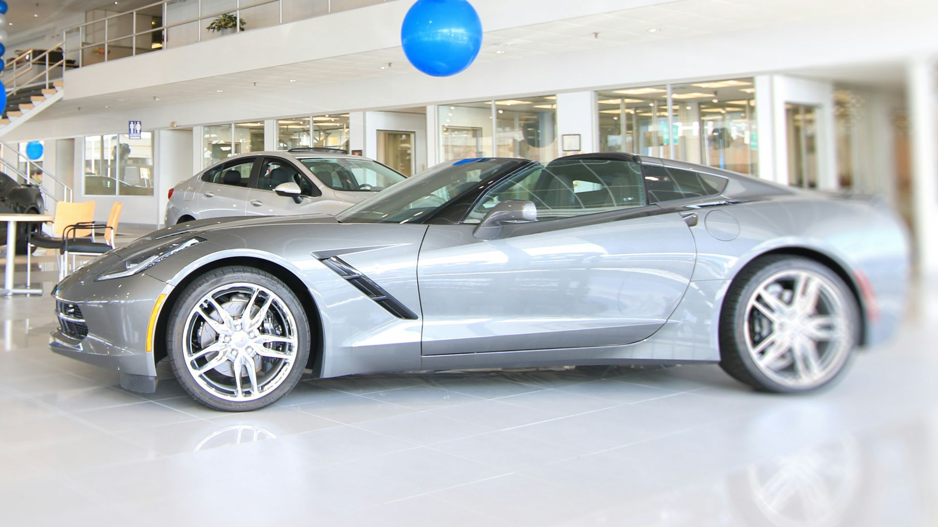 a silver sports car in a showroom with blue and white balloons