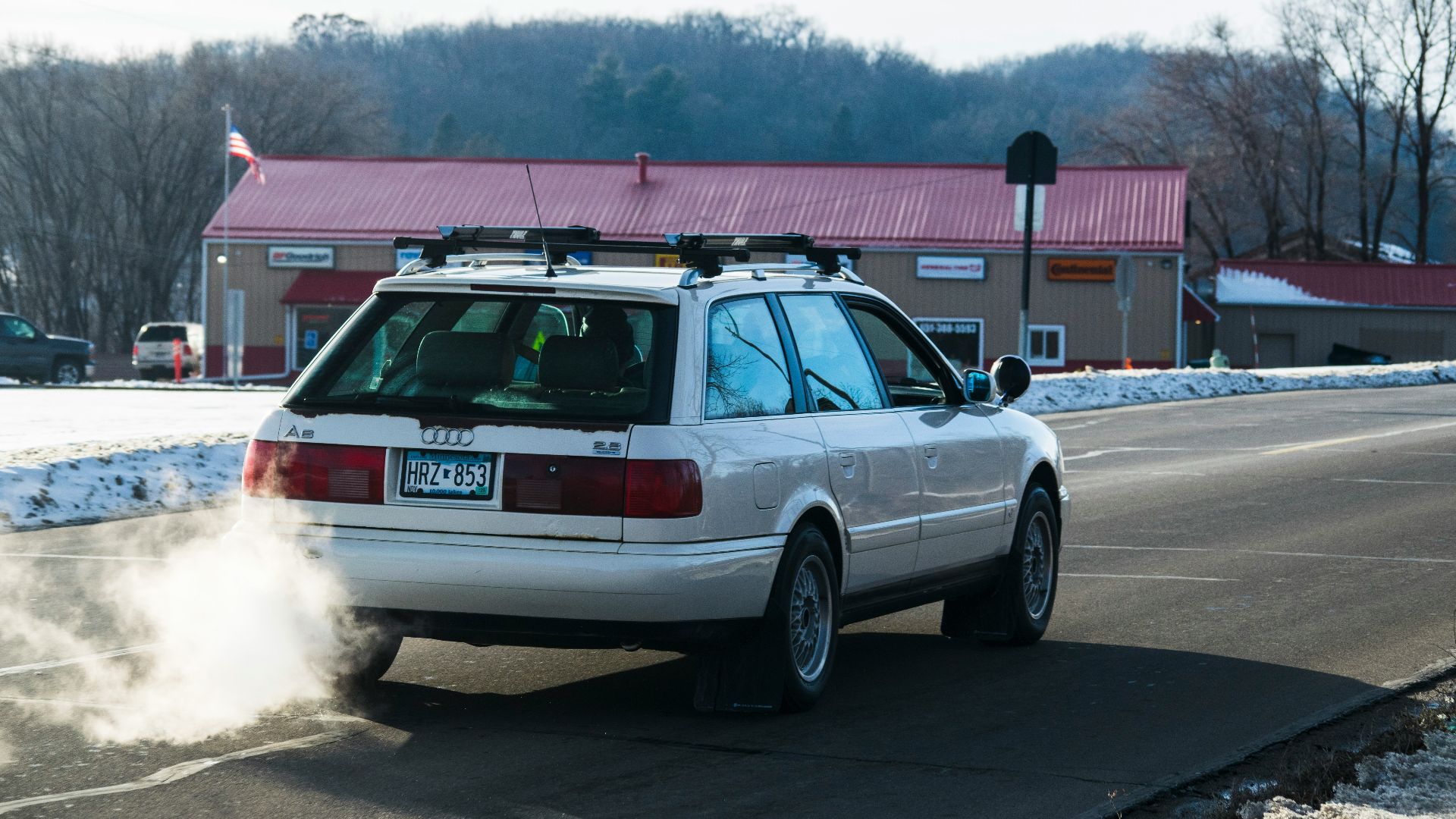 A white station wagon spews smoke while driving.