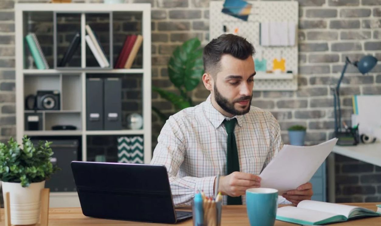 Man in Shirt Sitting at Office and Reading Document
