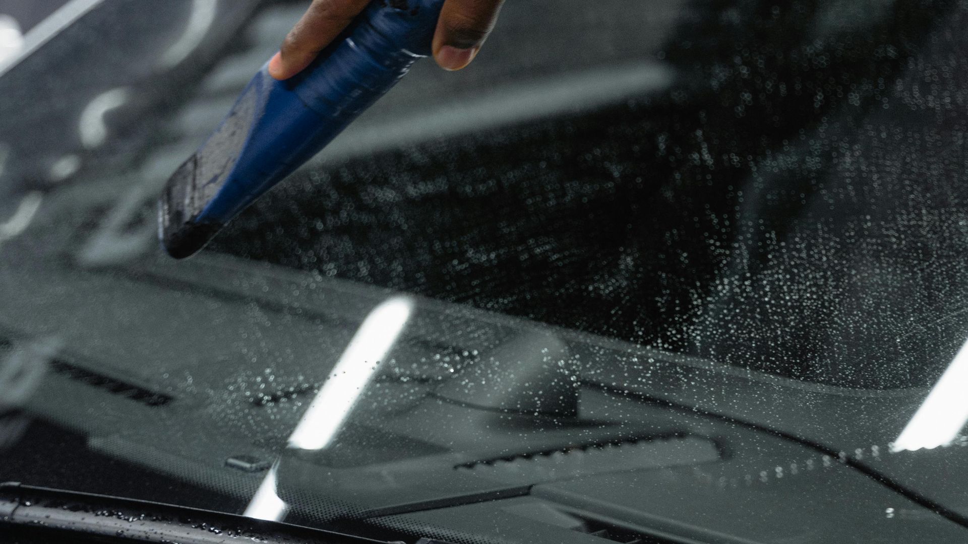 Close-up of a hand using a blower tool to dry a car windshield at an indoor carwash.