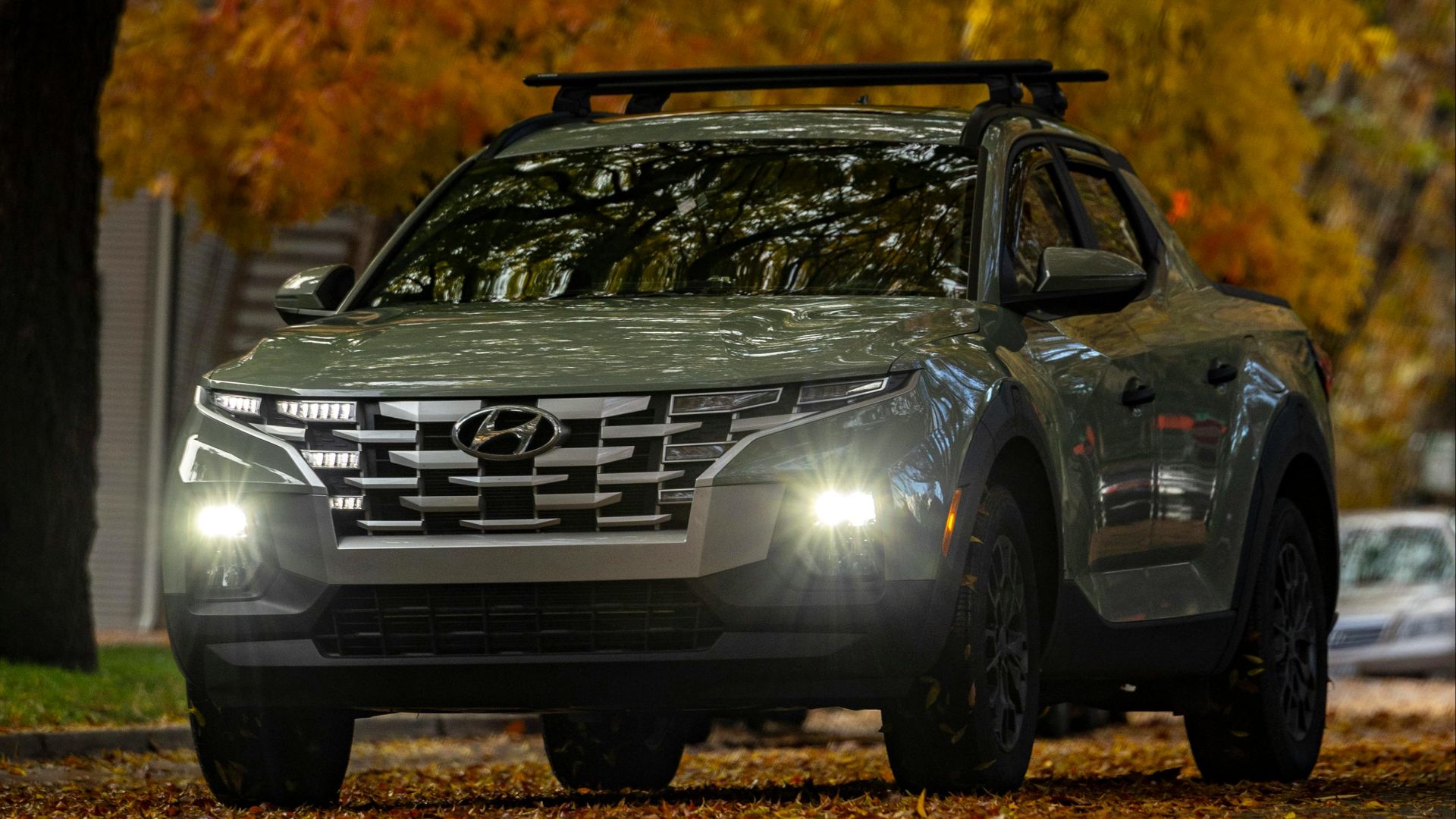 Silver pickup truck driving through a tree-lined road with golden autumn leaves.