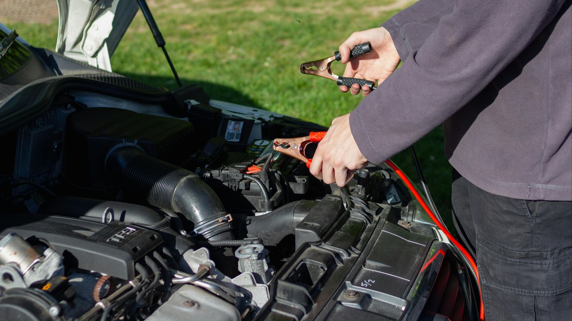 Close-up of mechanic using jumper cables to jump-start a car battery outdoors.