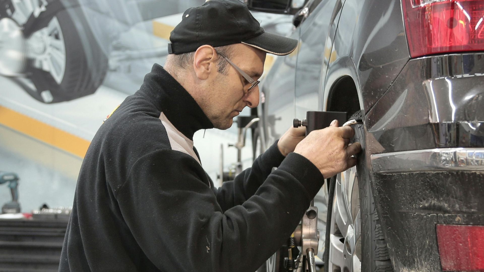 Side view of a mechanic aligning a car tire in a professional auto workshop.