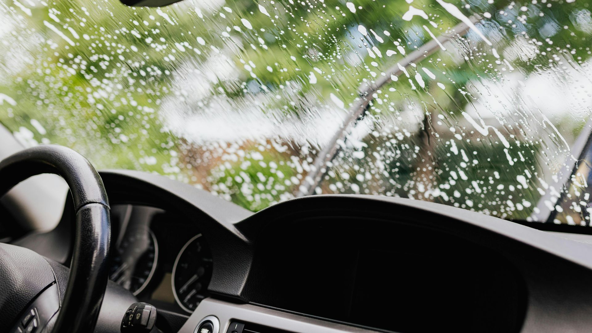 Interior view of a car with soapy windshield during cleaning. Clear dashboard visible.